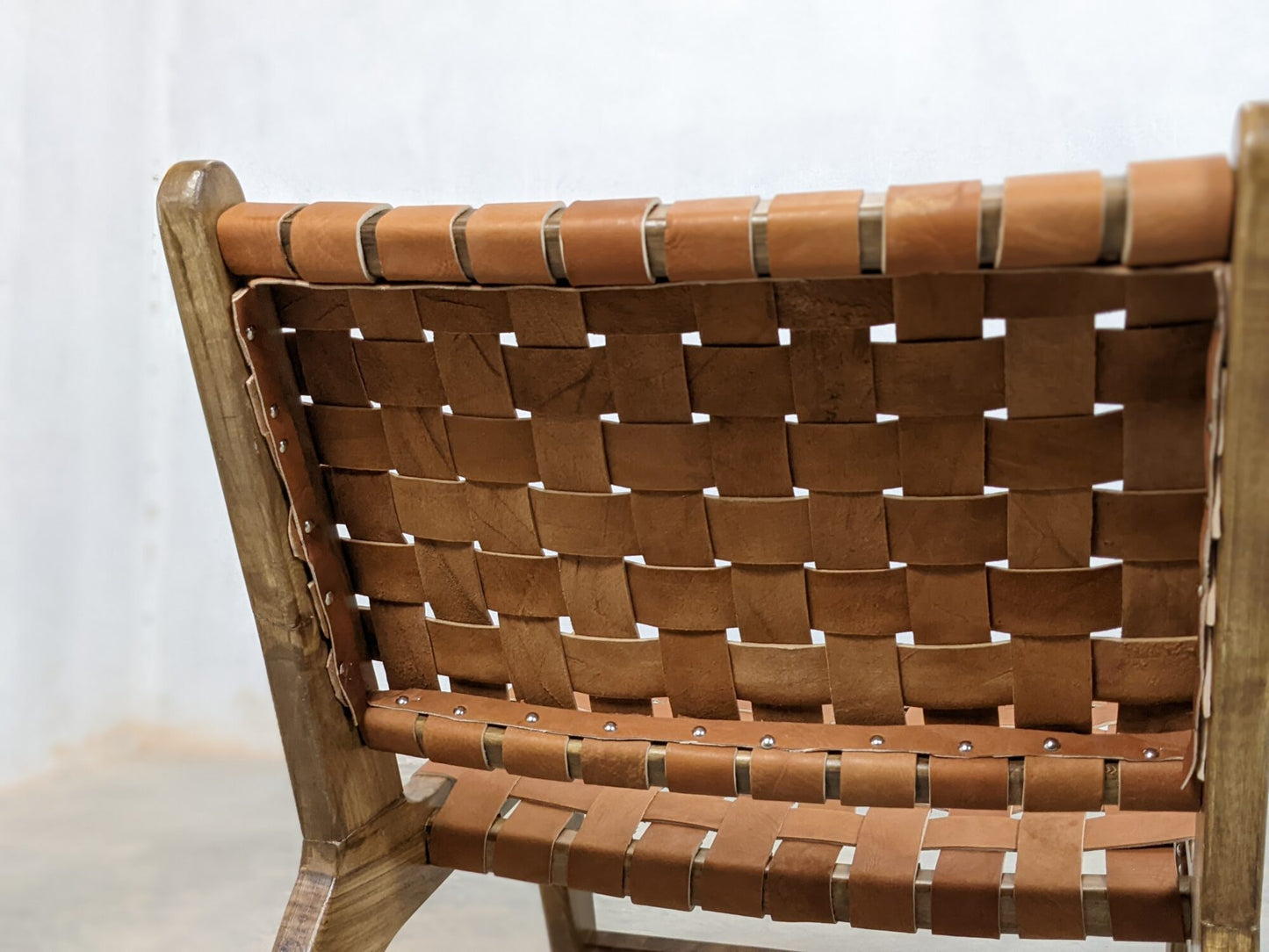 Wooden frame lounge chair featuring brown leather straps and artisan craftsmanship
